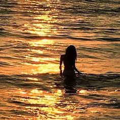 a woman is swimming in the ocean at sunset