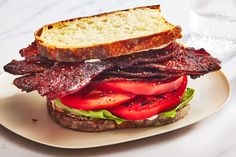 a sandwich with bacon, tomatoes and lettuce is on a plate next to a glass of water