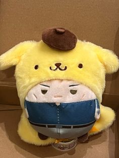 a yellow stuffed animal with a brown hat on it's head sitting in a cardboard box