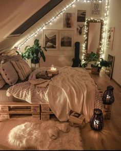 a bed with lots of pillows and blankets in a room that has lights on the wall