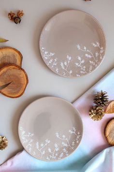 two white plates sitting on top of a table next to wooden slices and pine cones