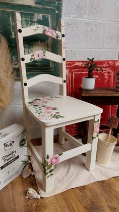 a white chair with pink flowers painted on the seat and back, sitting next to other items