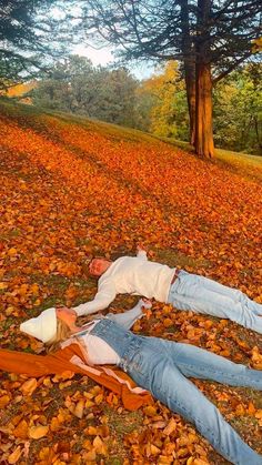 two people laying on the ground with leaves all over them and trees in the background