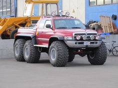 a large red truck parked in front of a blue building next to a yellow bulldozer