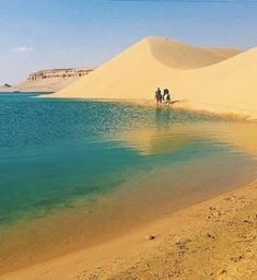 two people are riding horses on the sand dunes by the water's edge,