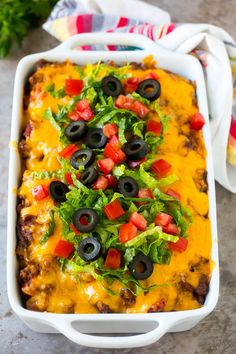 a white casserole dish filled with black olives, lettuce and tomatoes