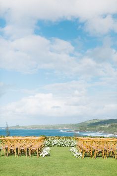 an outdoor ceremony setup with wooden chairs and flowers on the grass by the ocean in hawaii