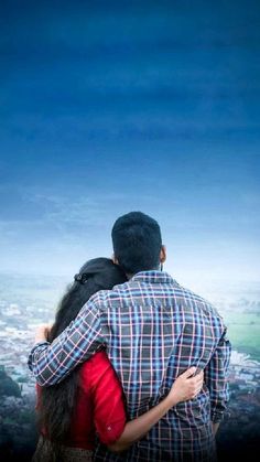 a man and woman embracing each other on top of a hill with a city in the background