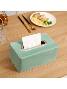 a tissue dispenser sitting on top of a wooden table next to plates and utensils