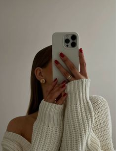 a woman taking a selfie with her cell phone in front of her face while wearing a white sweater