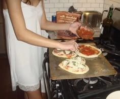 a woman is making homemade pizzas in the kitchen