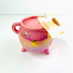 a pink and yellow ceramic pot with a tag on it's handle sitting on a white surface