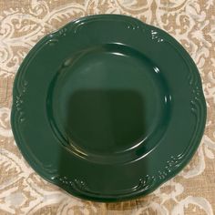 an empty green plate sitting on top of a tablecloth covered table with damask