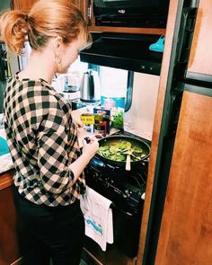 a woman standing in front of an open stove with food cooking on the burners