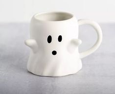 a white coffee cup with a ghost face on it's side and black eyes