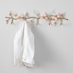 a white shirt hanging on a wall next to a coat rack with pink flowers and leaves