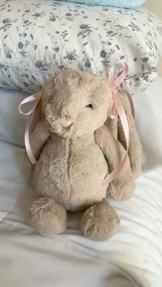 a stuffed rabbit sitting on top of a bed next to pillows and blankets with pink ribbons