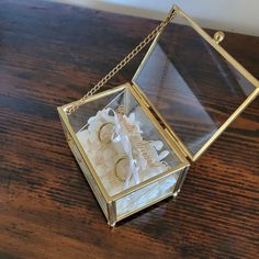 a glass box with two wedding rings inside on a wooden table, next to a chain