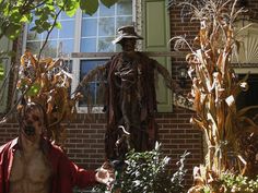 a scarecrow standing in front of a brick building next to a dead man statue