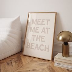 a white poster with the words meet me at the beach next to a lamp and books