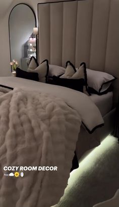 a bedroom with a large bed covered in white blankets and black trimmings next to a mirror