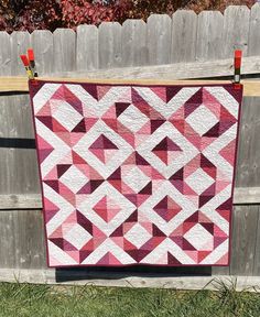 a pink and white quilt hanging on a fence