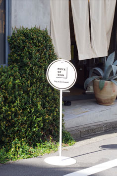 a white sign sitting on the side of a road next to a potted plant