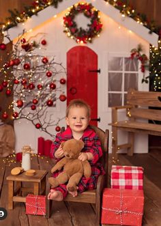 a little boy sitting on a chair holding a teddy bear in front of a christmas tree