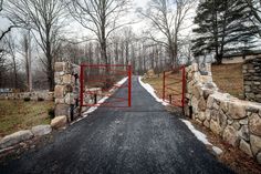 a gated driveway leading to a stone and brick house in the woods with snow on the ground