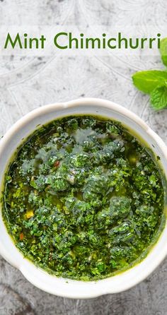 a white bowl filled with green pesto next to fresh basil leaves on top of a table