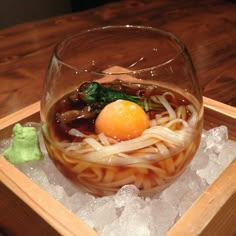 a bowl filled with noodles and an egg on top of ice in a wooden tray