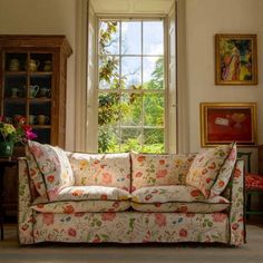 a couch sitting in front of a window next to a wooden table with flowers on it