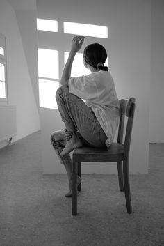 a man sitting on top of a wooden chair in an empty room next to a window