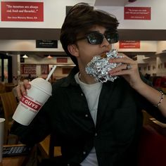 a young man is eating and drinking from a paper cup while sitting in a restaurant