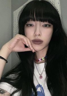 a woman with long black hair wearing a white t - shirt and colorful necklaces