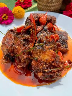 a white plate topped with meat covered in sauce and garnished with flowers on the side