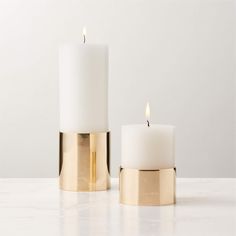 two white candles sitting on top of a table next to each other with gold trim