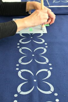 a woman is painting on a blue table cloth with white circles and dots in the center