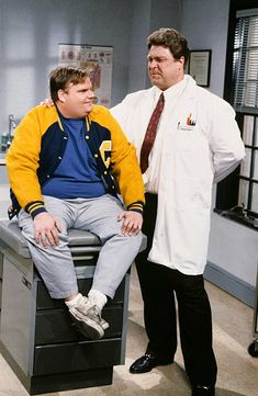 two men in lab coats standing next to each other and one is sitting on a desk