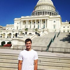 a young man standing in front of the capitol building with steps leading up to it