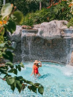 a woman in a red swimsuit and straw hat standing in a pool with waterfall