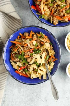 two blue bowls filled with stir fried vegetables and noodles next to some dipping sauces