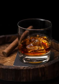 an old fashioned glass with ice and cinnamon on a wooden tray next to some cigars