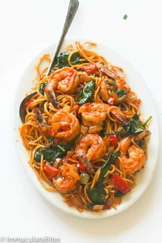 a white plate topped with pasta and shrimp on top of a bed of spinach