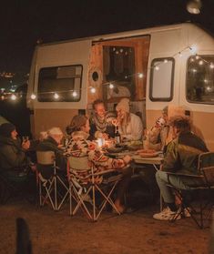 a group of people sitting around a table in front of a camper at night