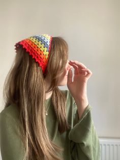 a woman with long hair wearing a colorful crochet hat and holding her hand to her face