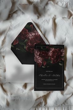 two black and white wedding cards with red flowers on the front one is folded in an envelope