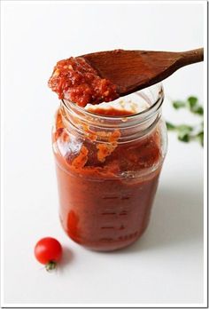 a wooden spoon full of sauce on top of a jar filled with tomato paste and parsley