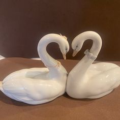 two white swans sitting next to each other on top of a brown cloth covered ground