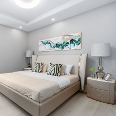 a large white bed sitting in a bedroom next to a painting on the wall above it